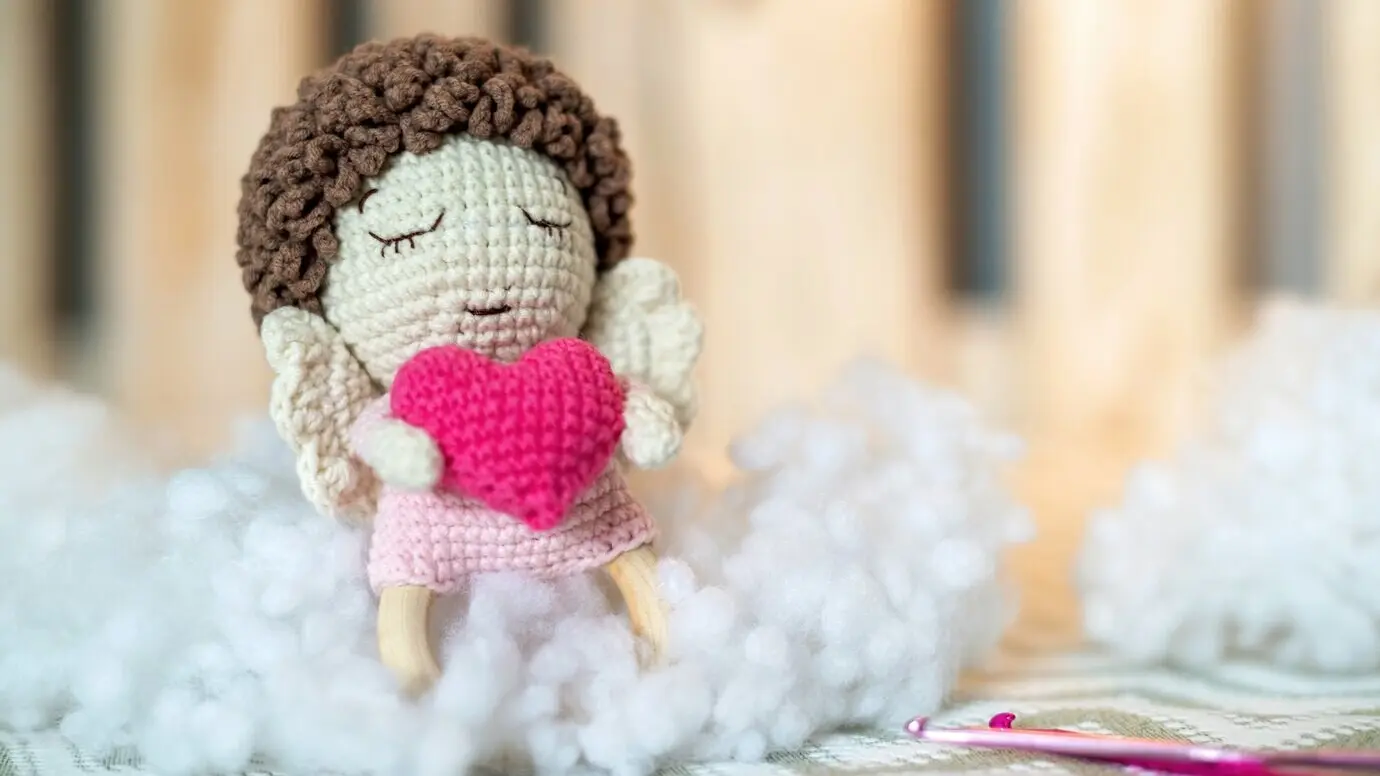 Niedliches gestricktes Kuscheltier auf dem Sofa, umgeben von Plüsch.