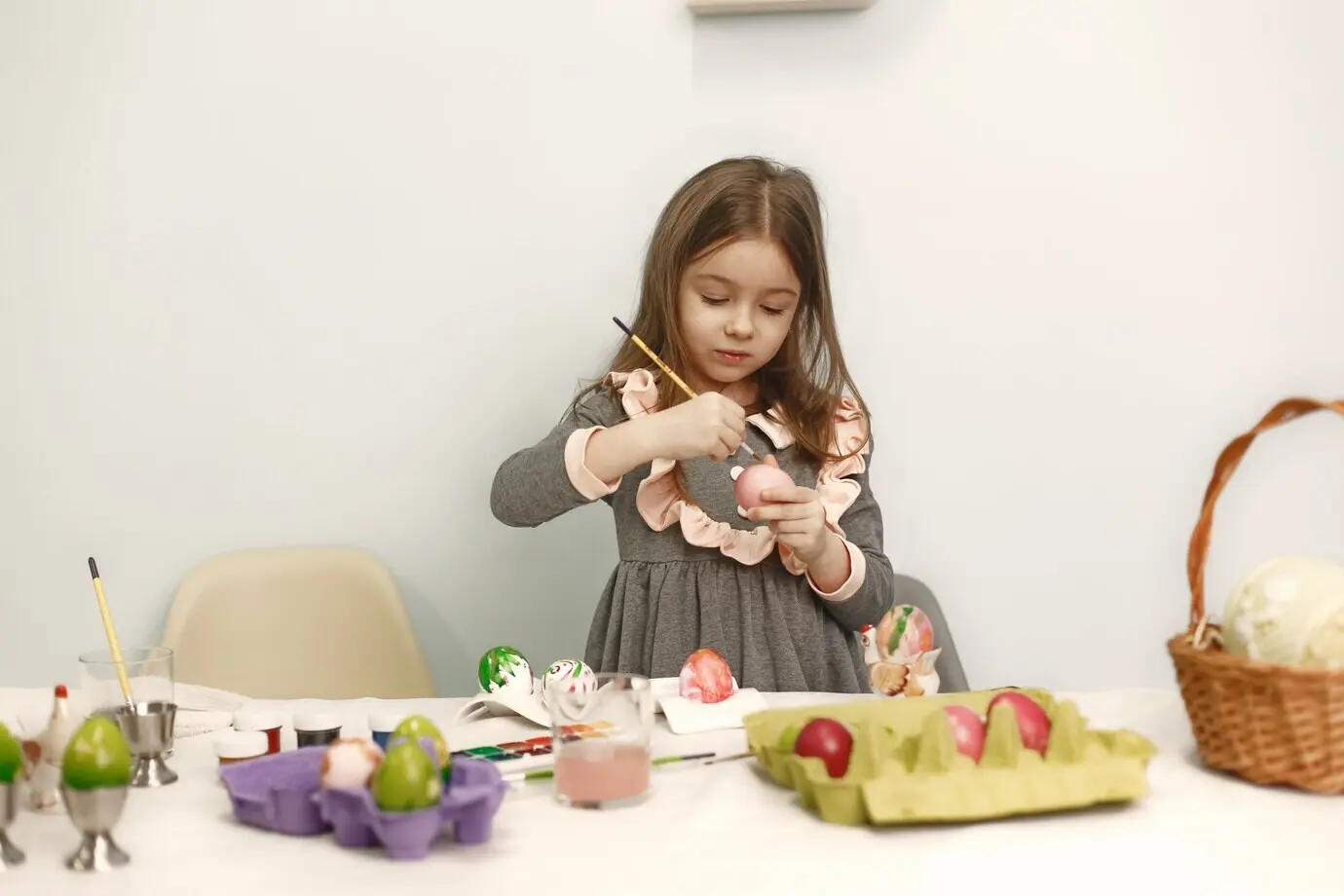 Ein niedliches kleines Mädchen bemalt Eier. Die Familie sitzt zu Hause. Sie bereitet sich auf Ostern vor.